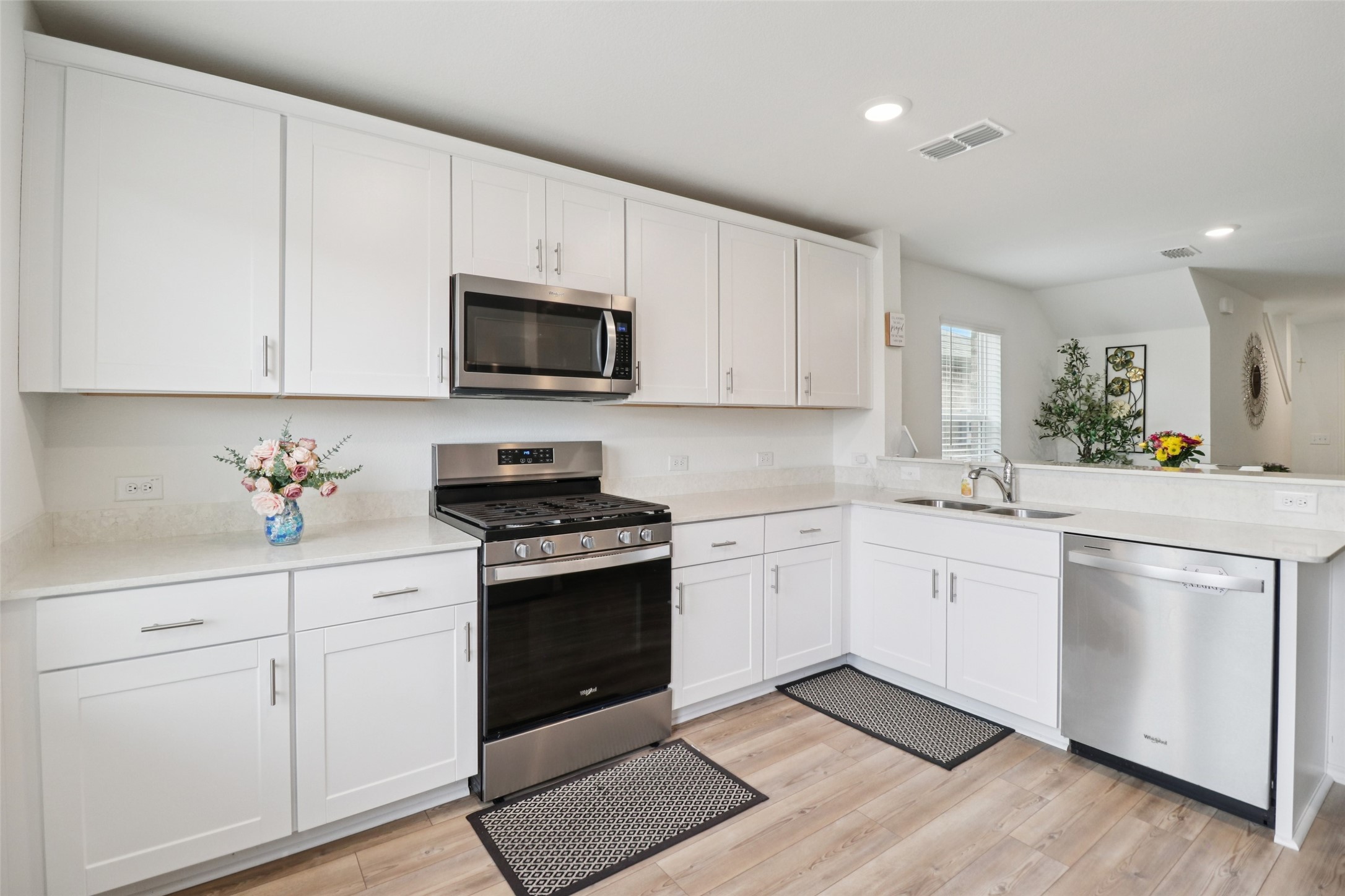 Bright white kitchen with stainless-steel appliances, light counters, and wood-look floors.