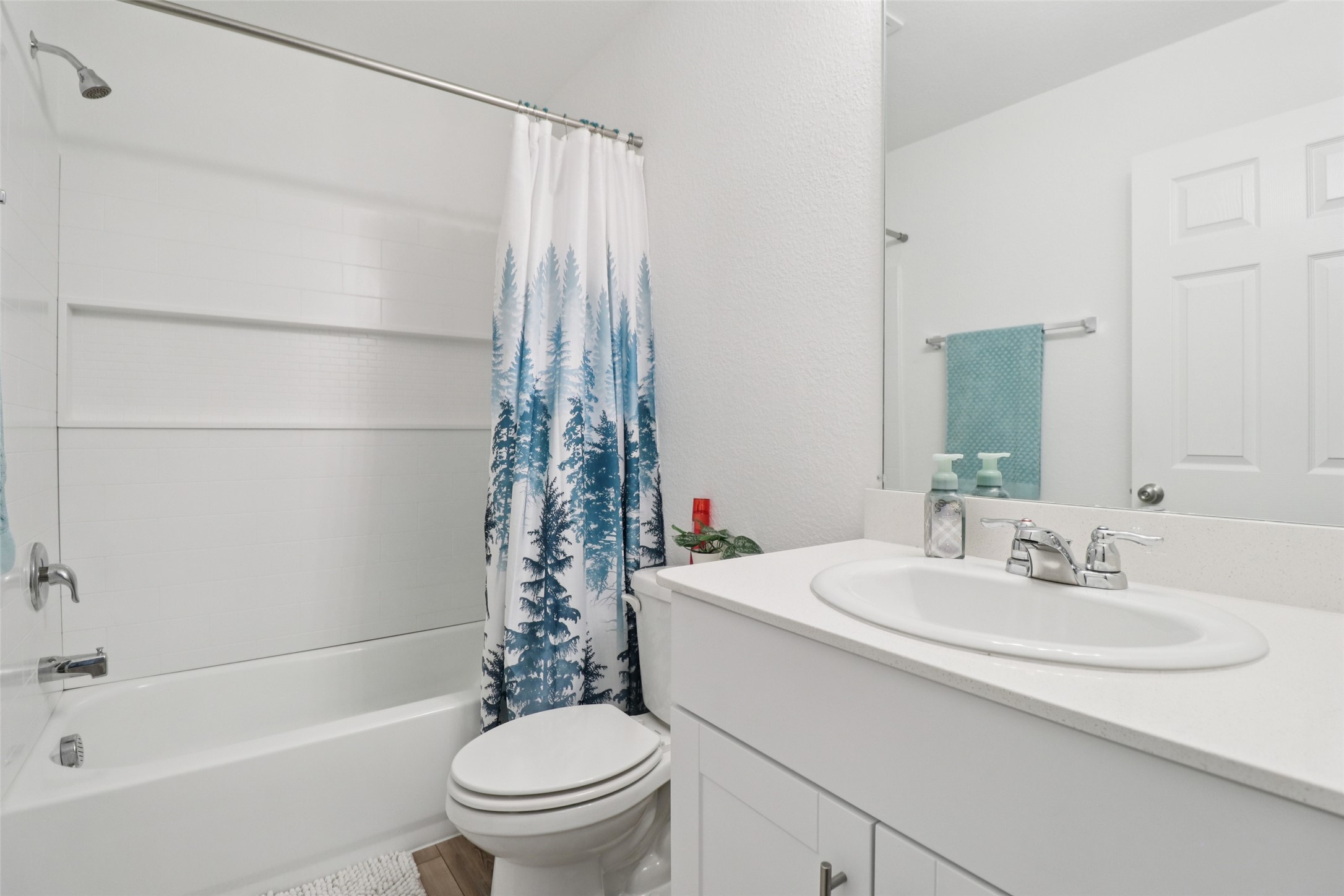 Bathroom with a white tub, blue forest-pattern shower curtain, toilet, and vanity sink.