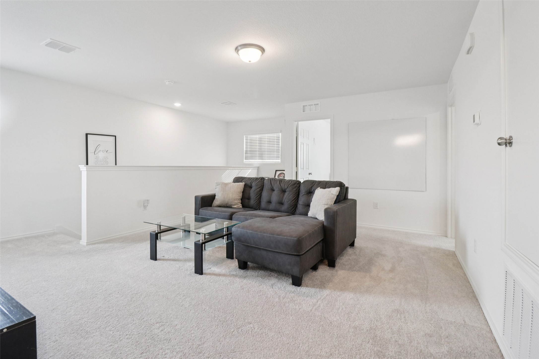 Upstairs living room with a dark gray sectional, glass coffee table, and large whiteboard.