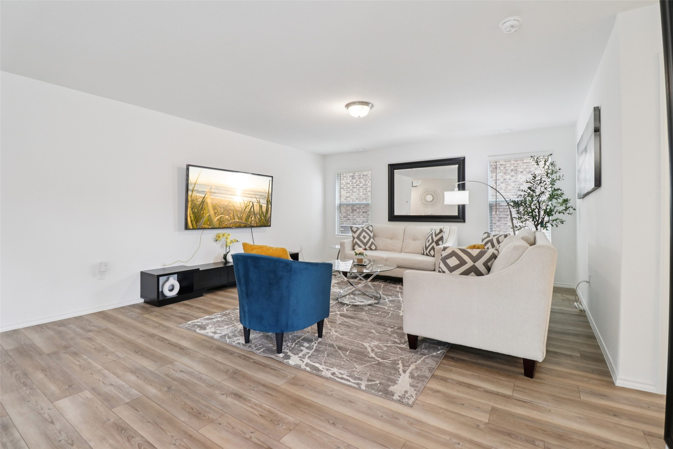 Staged living room with cream sofas, a blue accent chair, and light wood flooring.