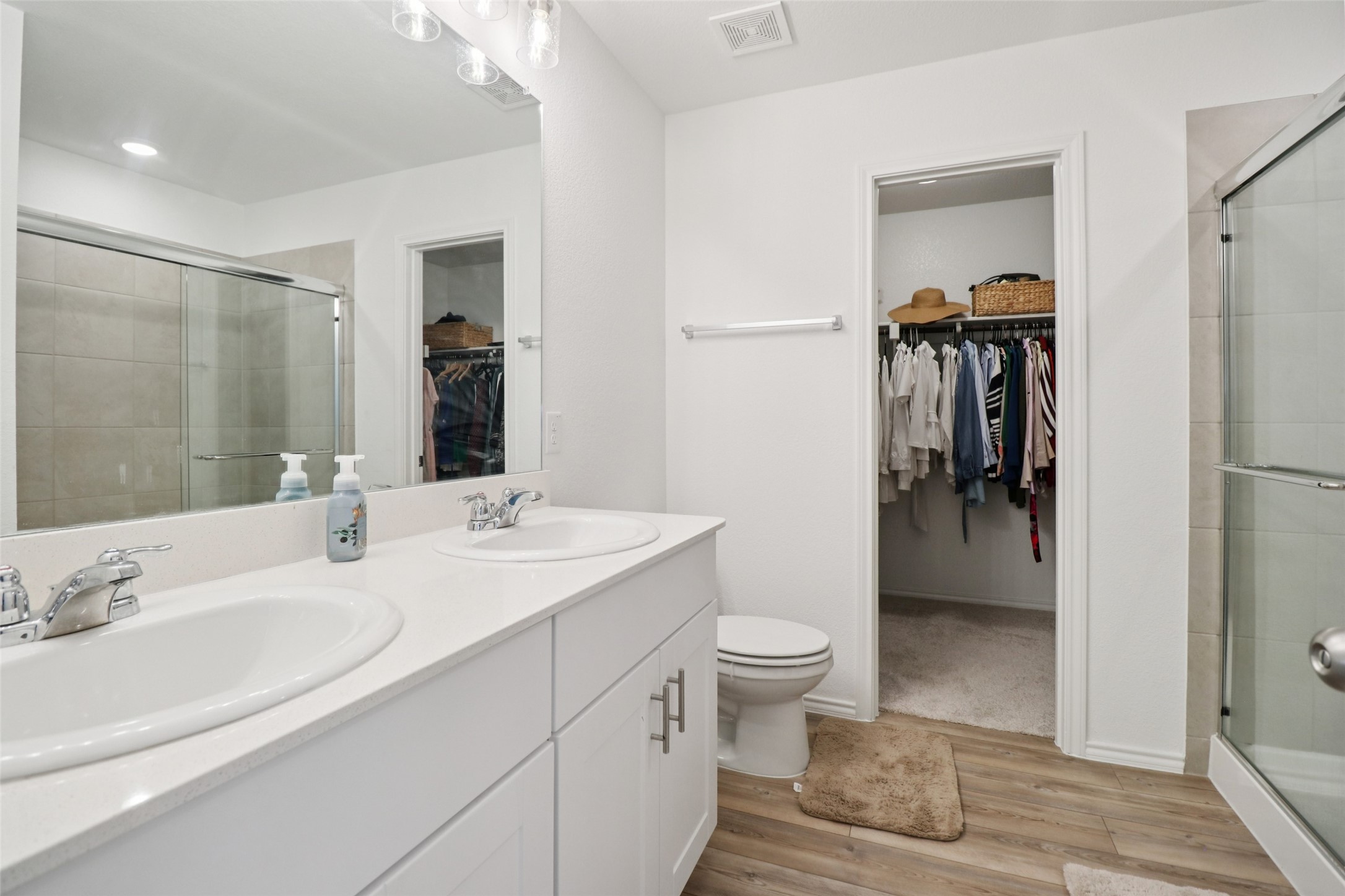 Bathroom with double-sink vanity, glass shower, and doorway opening to a walk-in closet.