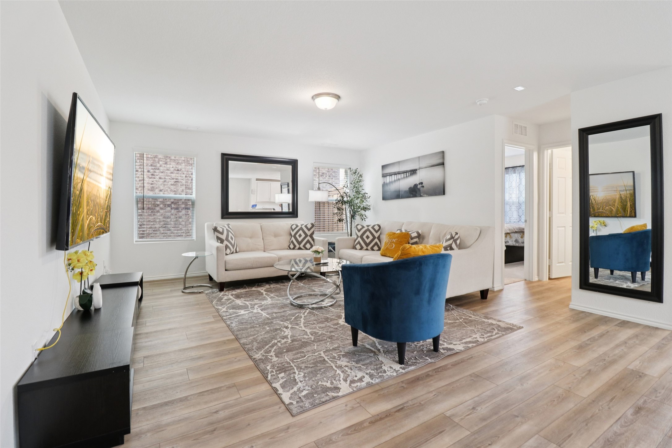 Staged living room with cream sofas, a blue accent chair, and light wood floors.