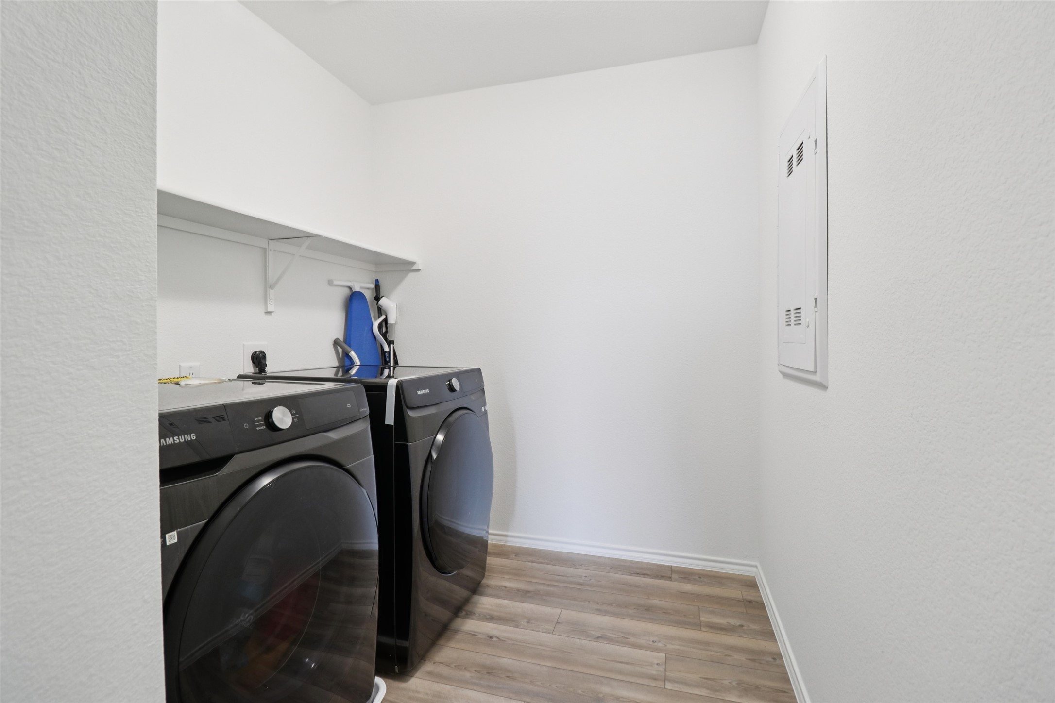 Laundry room with black washer and dryer, a wall shelf, and light wood-look flooring.