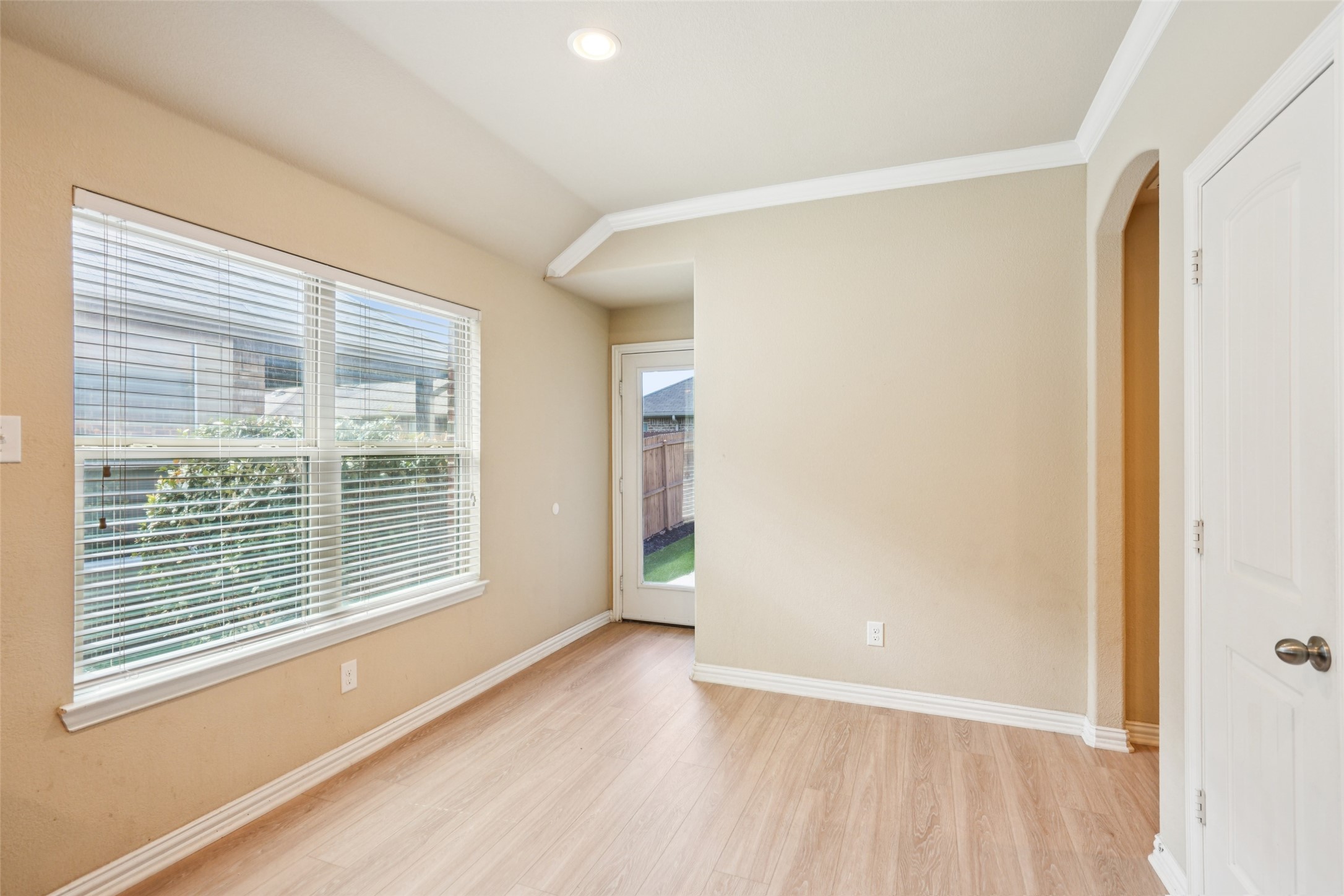 Vacant room with wood-look floors, a large blinded window, and a glass-paneled exterior door.