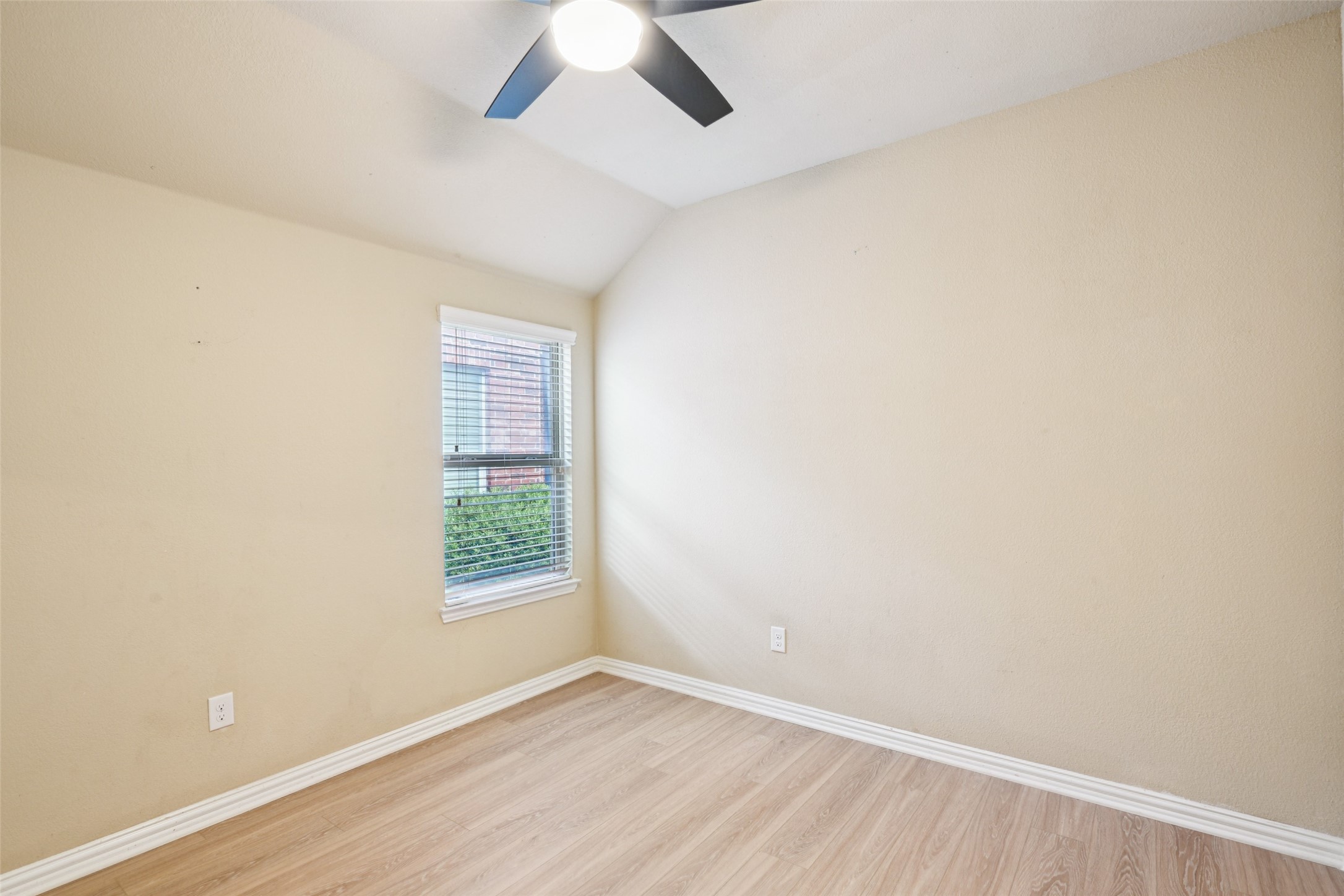 Empty room with light wood flooring, a high angled ceiling, and a window with white blinds.