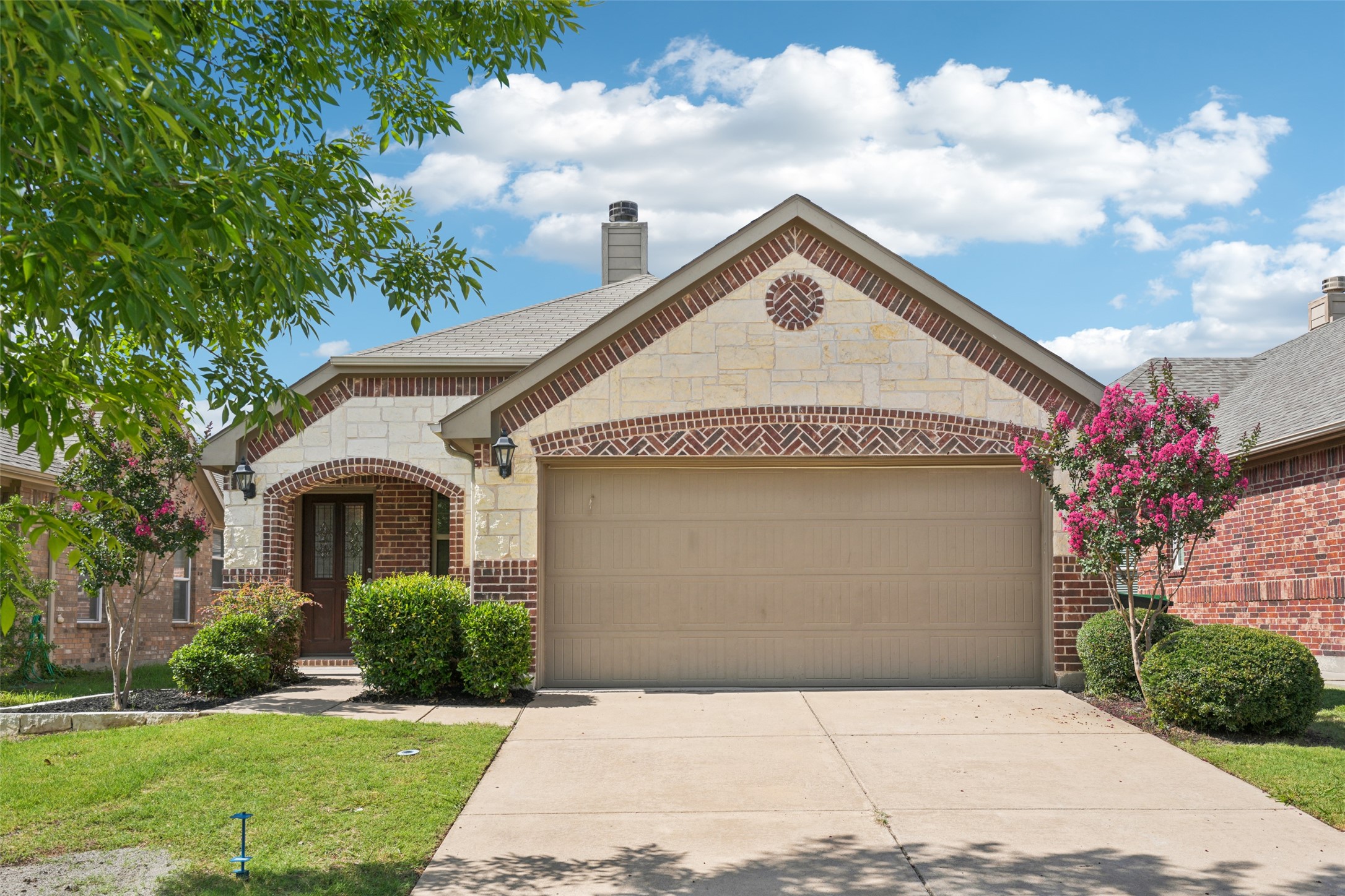Single-story stone and brick home with a two-car garage and pink flowering trees.