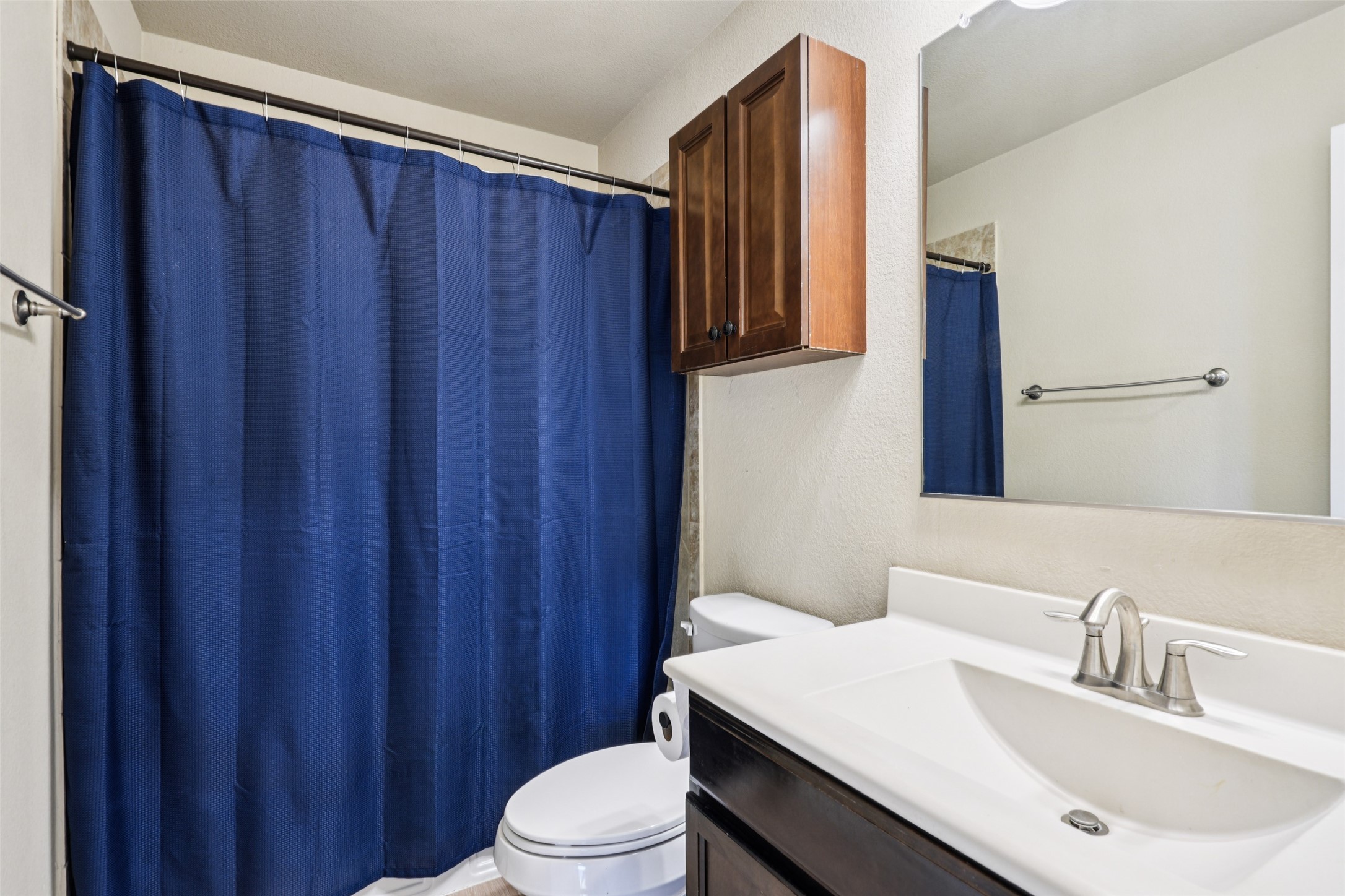 Bathroom with a blue shower curtain, dark wood vanity, white sink, and large mirror.