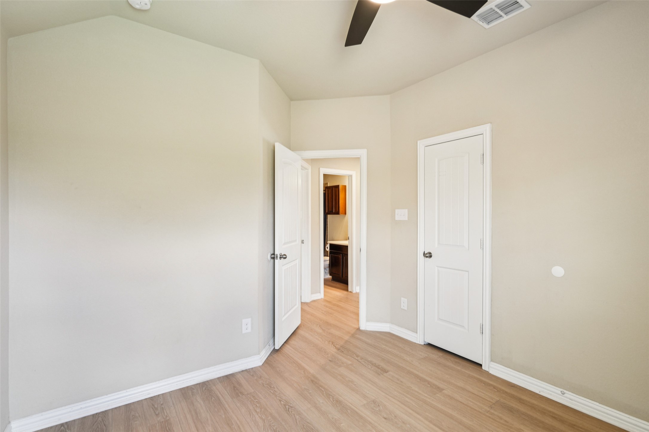 Empty bedroom with wood-look flooring and an open doorway to a bathroom vanity.