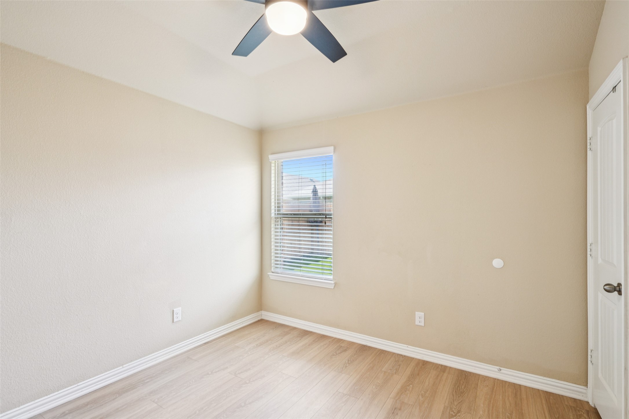 Empty room with light wood-look flooring, a ceiling fan, and a window with blinds.