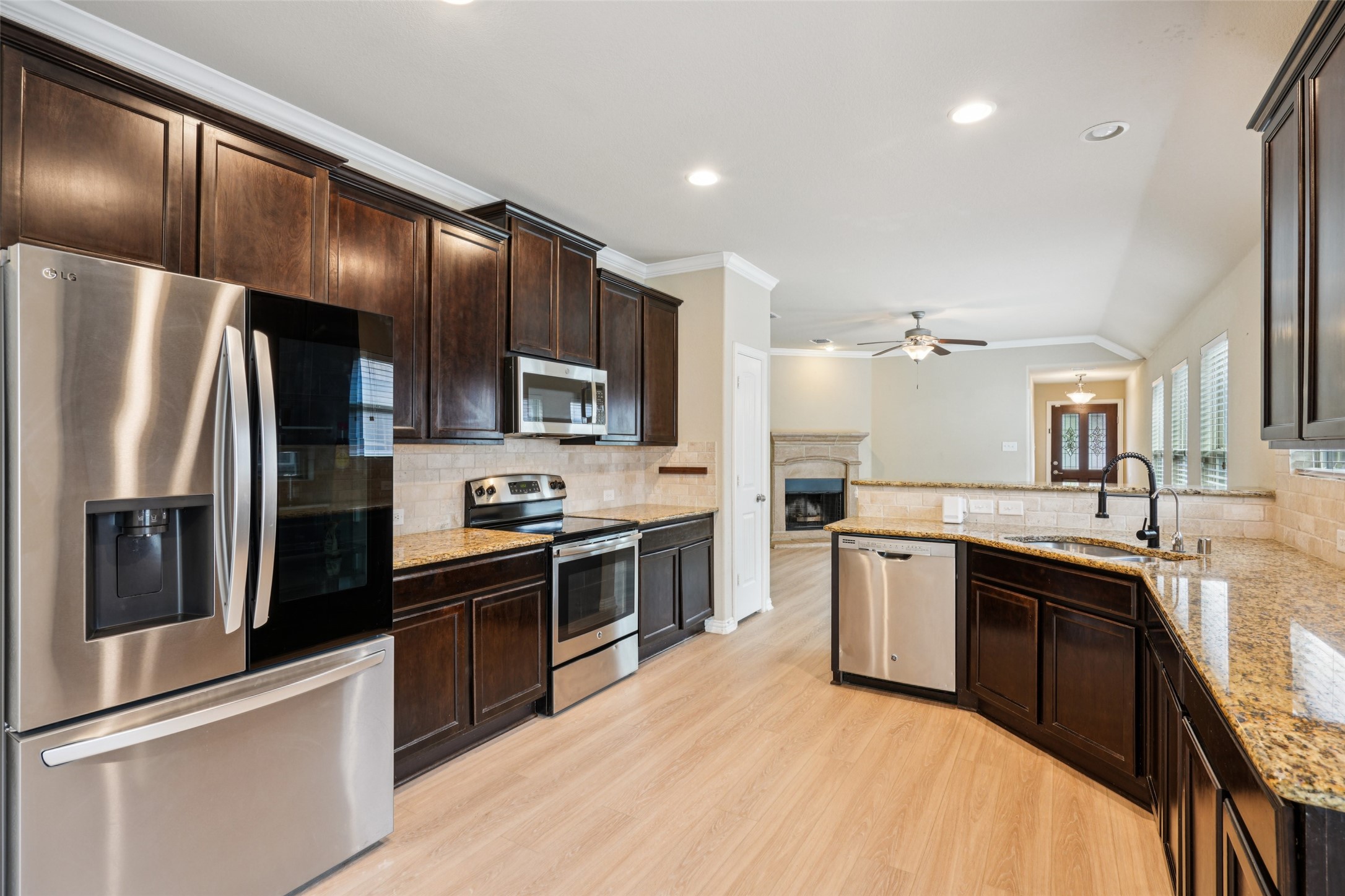 Kitchen with dark wood cabinets, granite counters, stainless steel appliances, and an island sink.