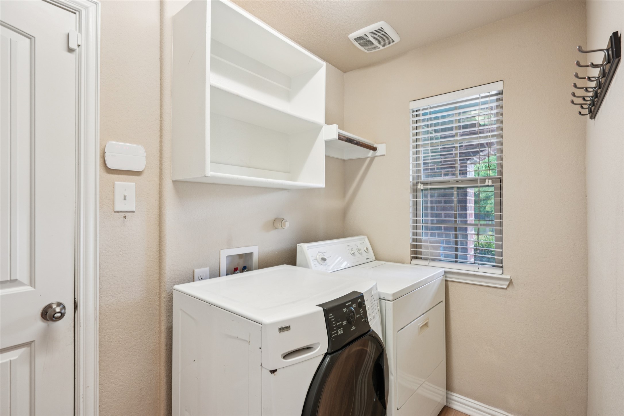 Laundry room with a front-loading washer and dryer beneath open shelving.