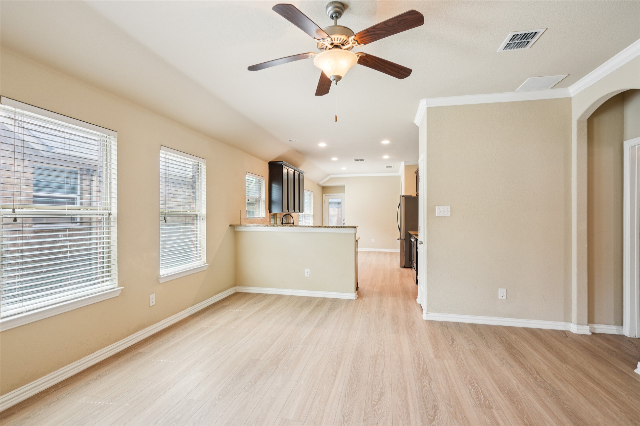 Vacant dining area opening to the kitchen, with large windows and light wood-look flooring.