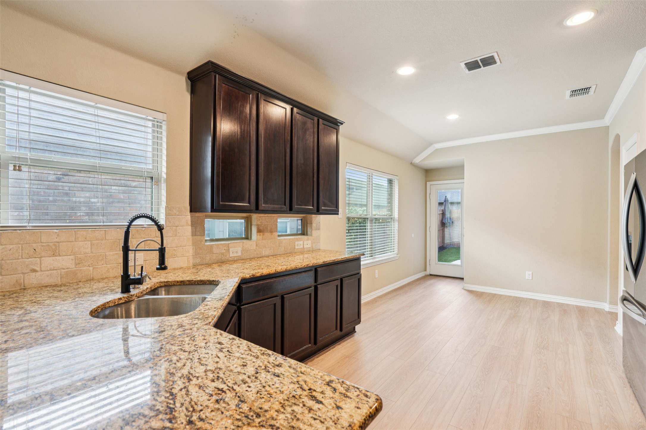 Vacant kitchen with dark wood cabinets, granite counters, and a stainless sink.