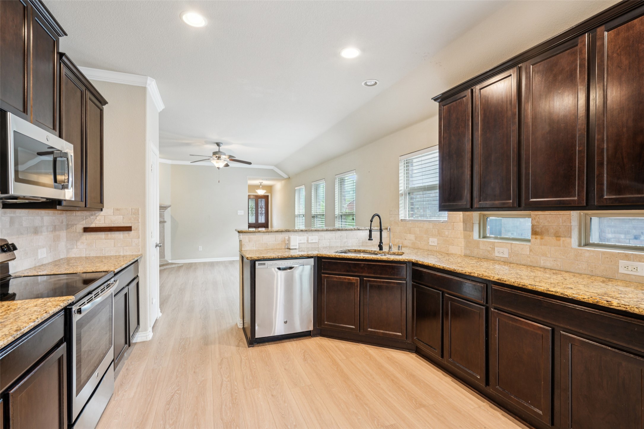 Kitchen with dark wood cabinets, granite counters, stainless steel appliances, and a peninsula sink.