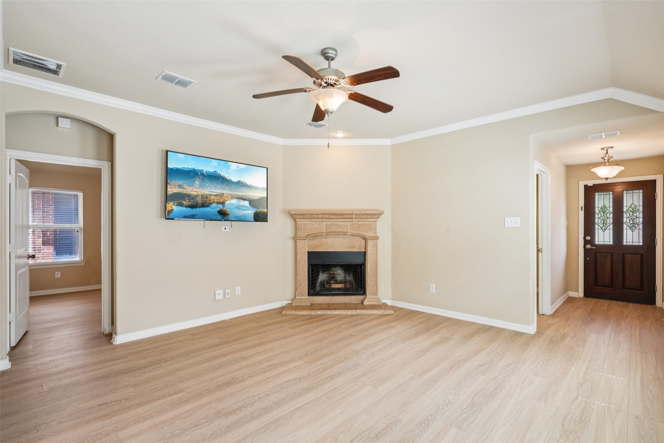 Vacant living room with a stone fireplace, wall-mounted television, and light wood floors.