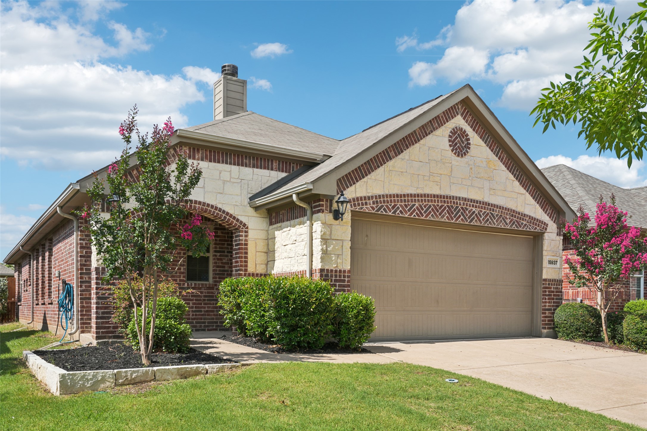 Brick and stone house with a tan double garage door and flowering trees in the front yard.