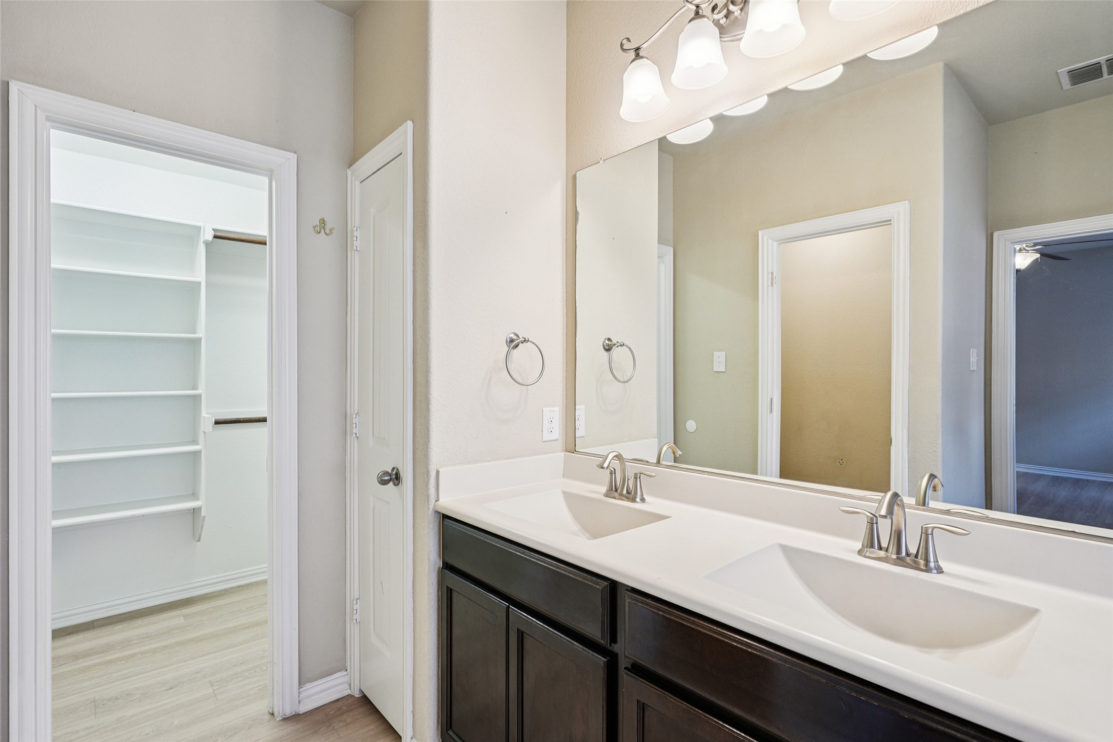 Bathroom with a double-sink vanity and mirror beside a walk-in closet with built-in shelves.