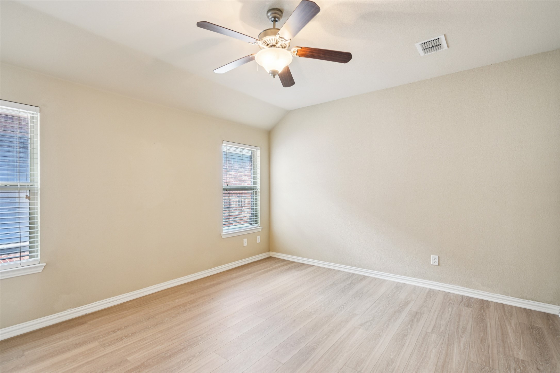 Empty room with wood-look flooring, two windows with blinds, and a ceiling fan.