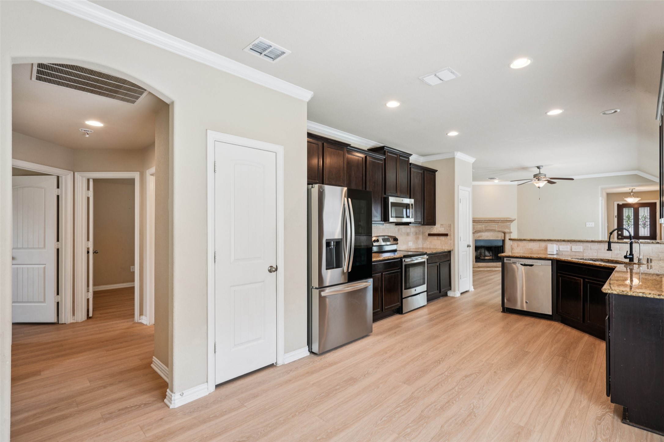 Kitchen with dark wood cabinets, stainless steel appliances, and a granite island beside an open living area.