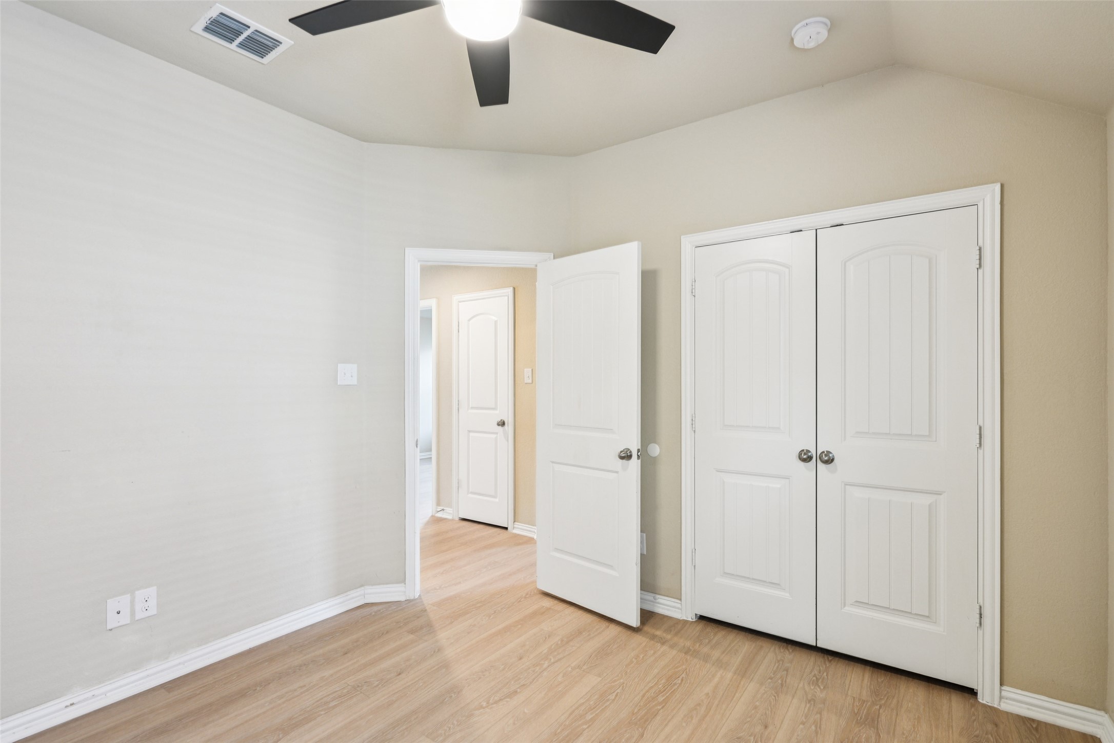 Empty bedroom with light wood floors, a ceiling fan, and double closet doors.