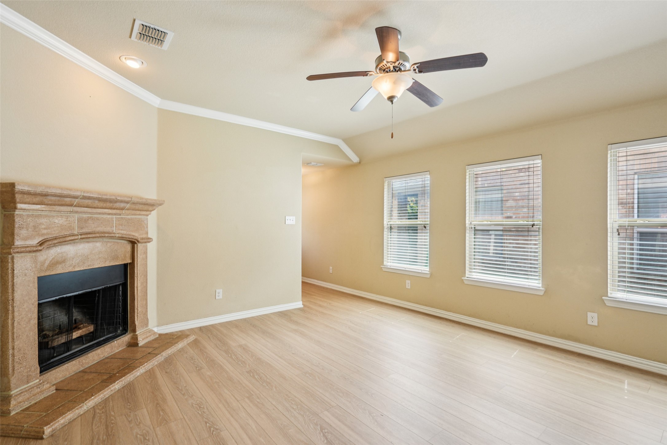 Empty living room with a stone fireplace, light flooring, and three windows with blinds.