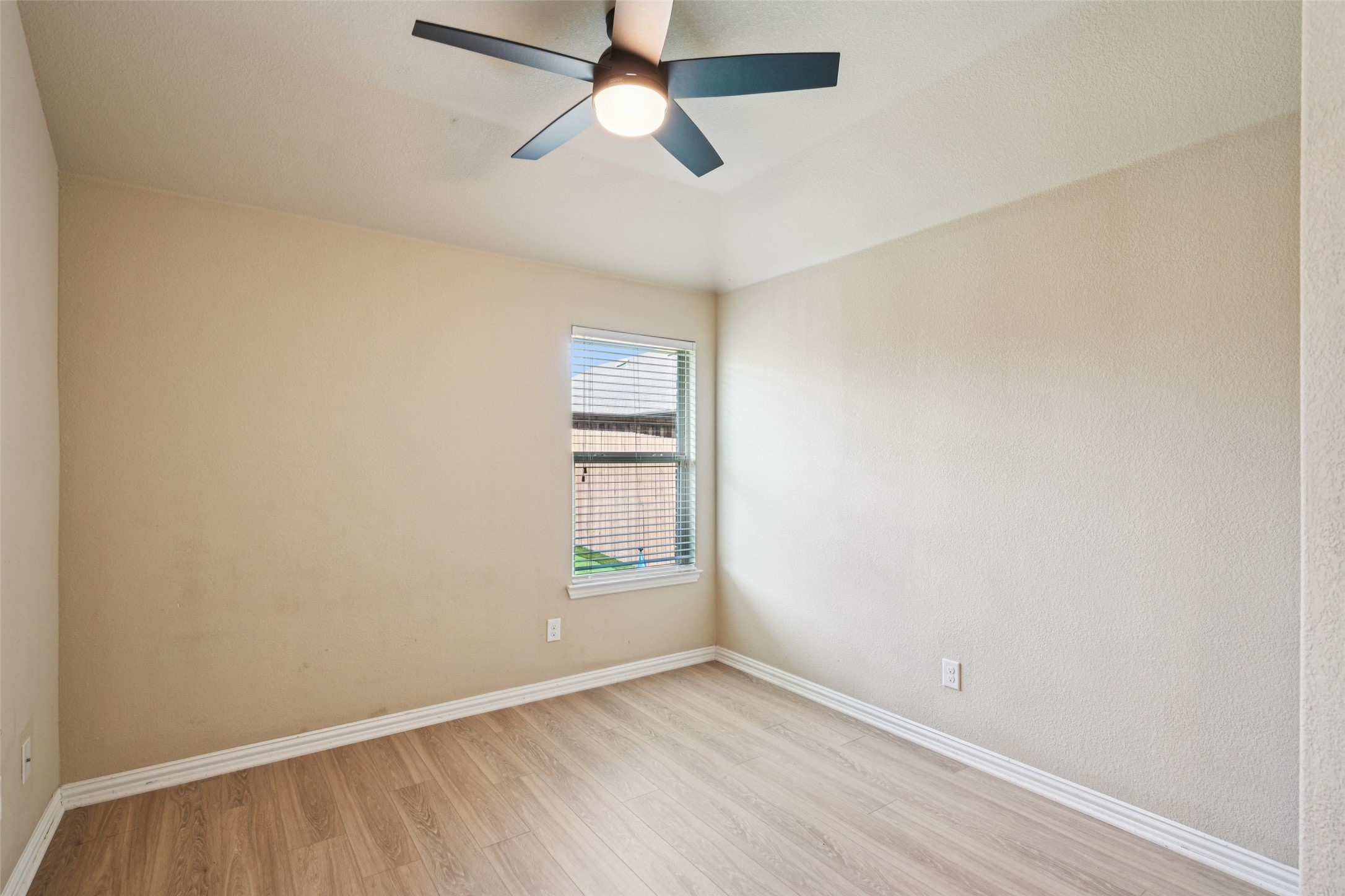 Empty bedroom with wood-look flooring, a window with blinds, and a ceiling fan.