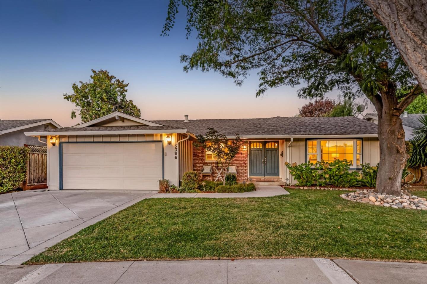 Single-story home with a two-car garage, brick entry accents, and a mature tree beside the lawn.