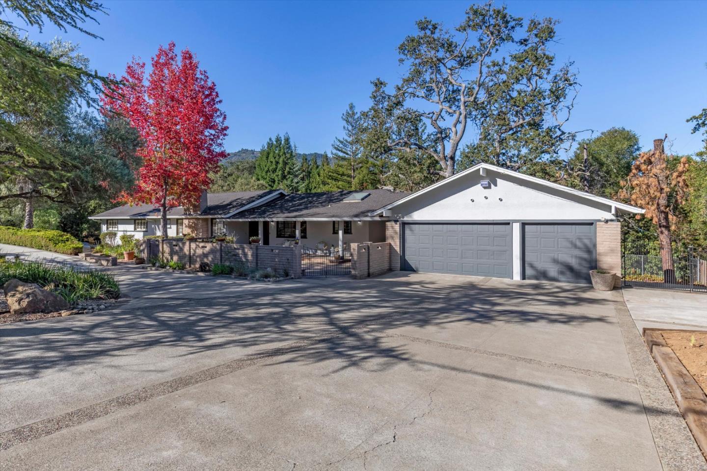 Single-story home with a two-car garage and broad driveway, framed by mature trees and red autumn foliage.