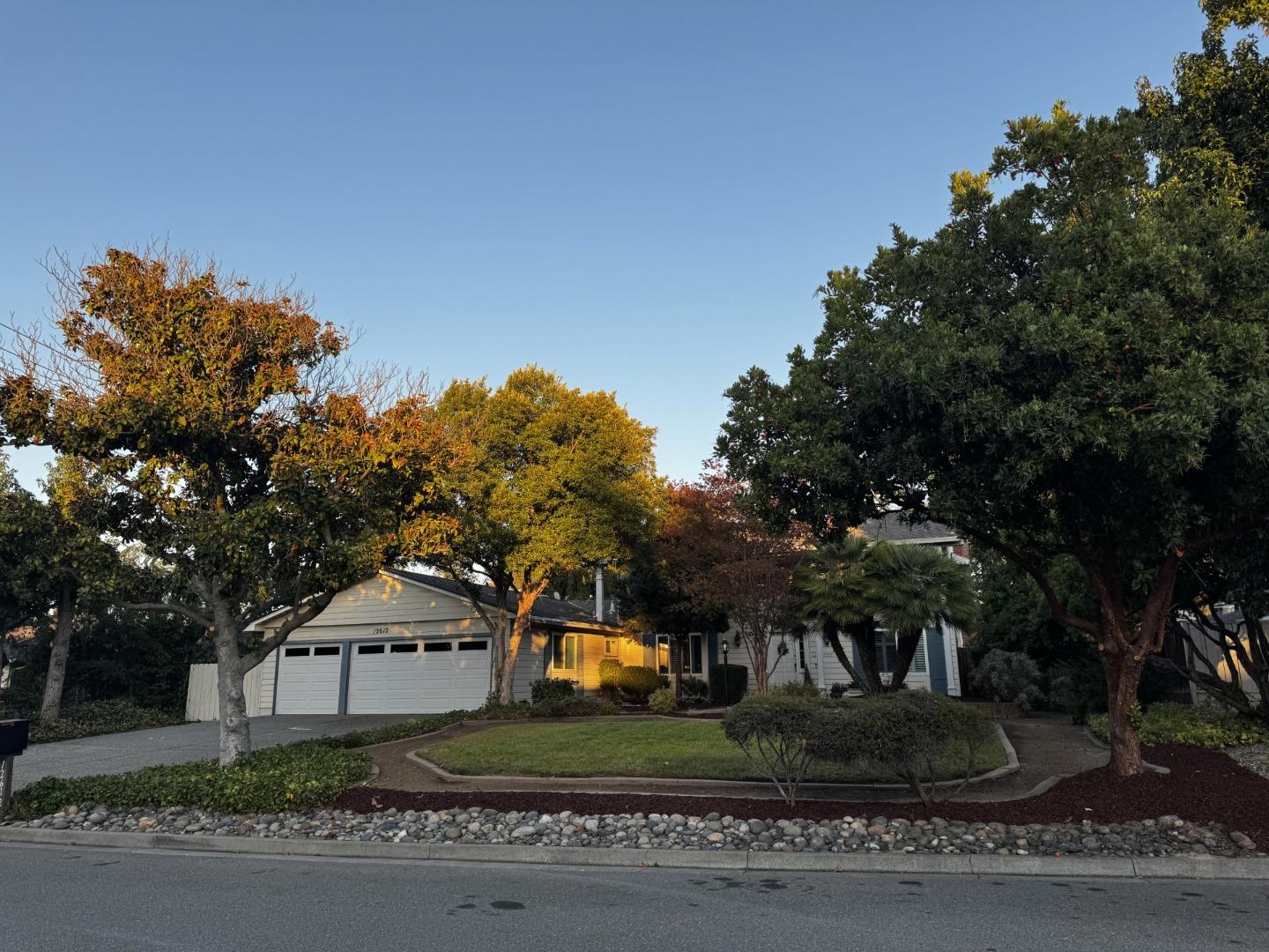 Suburban house partly screened by mature trees, with a double garage and landscaped front yard.