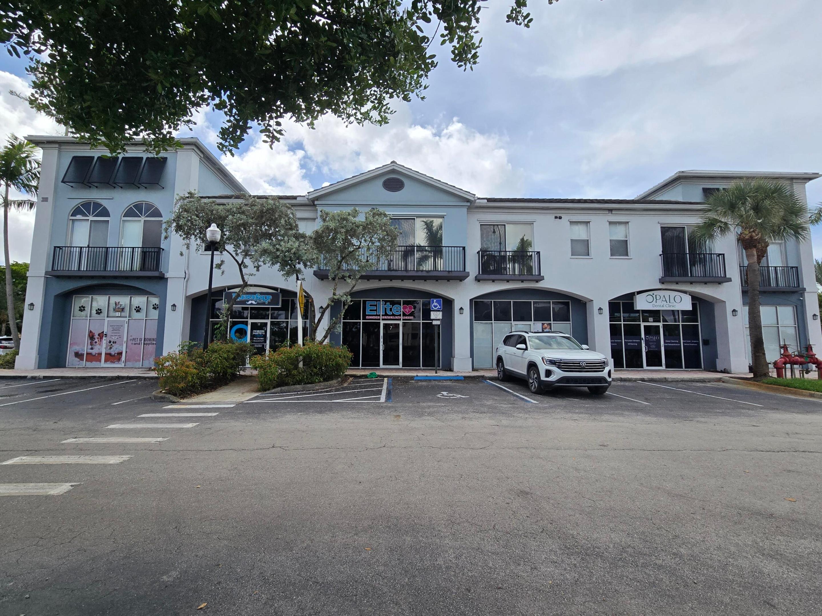 Two-story retail building with arched storefronts, balconies, and a white SUV in the parking lot.