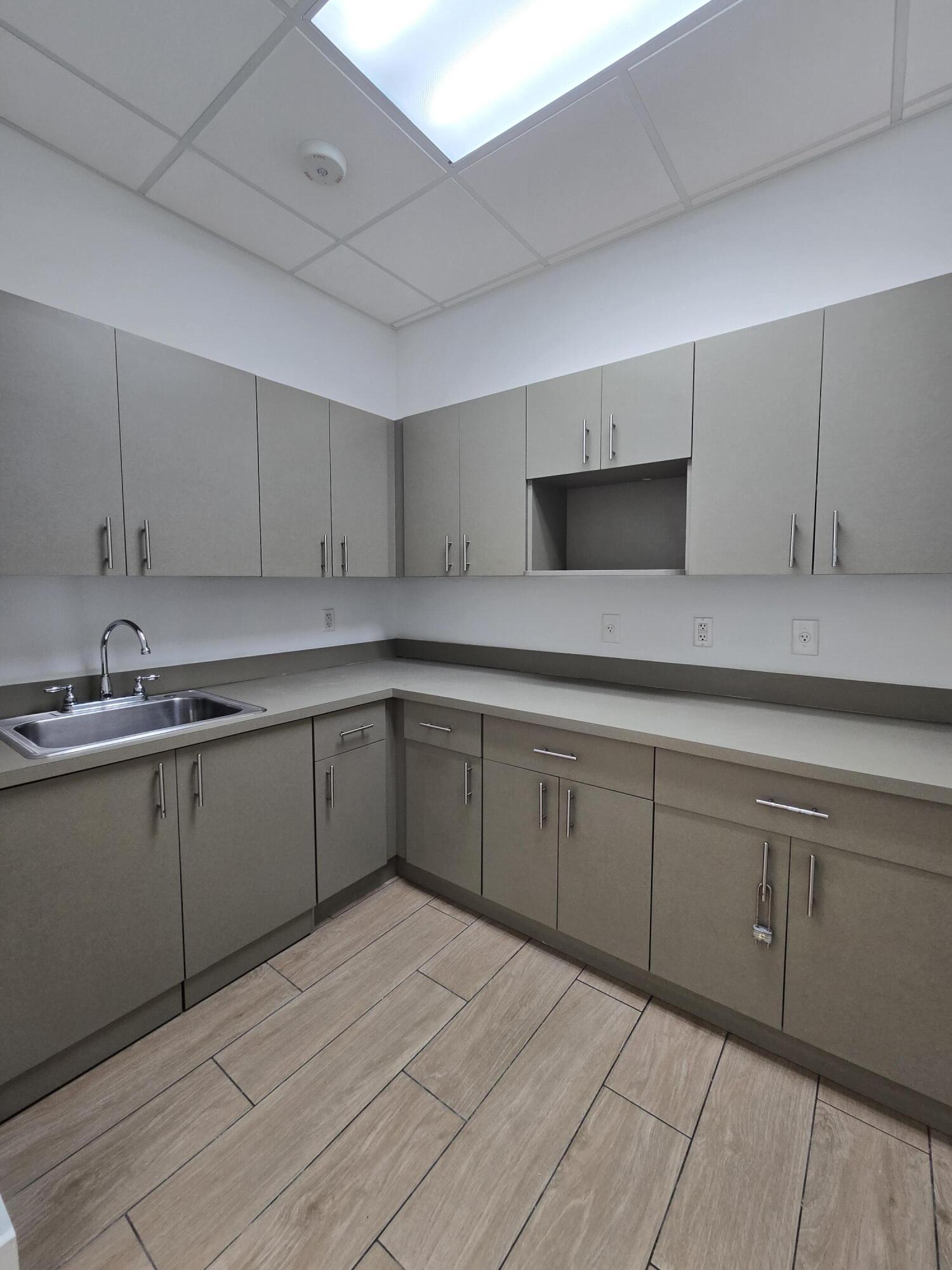 Empty kitchenette with gray cabinets, a stainless steel sink, and pale tile flooring.