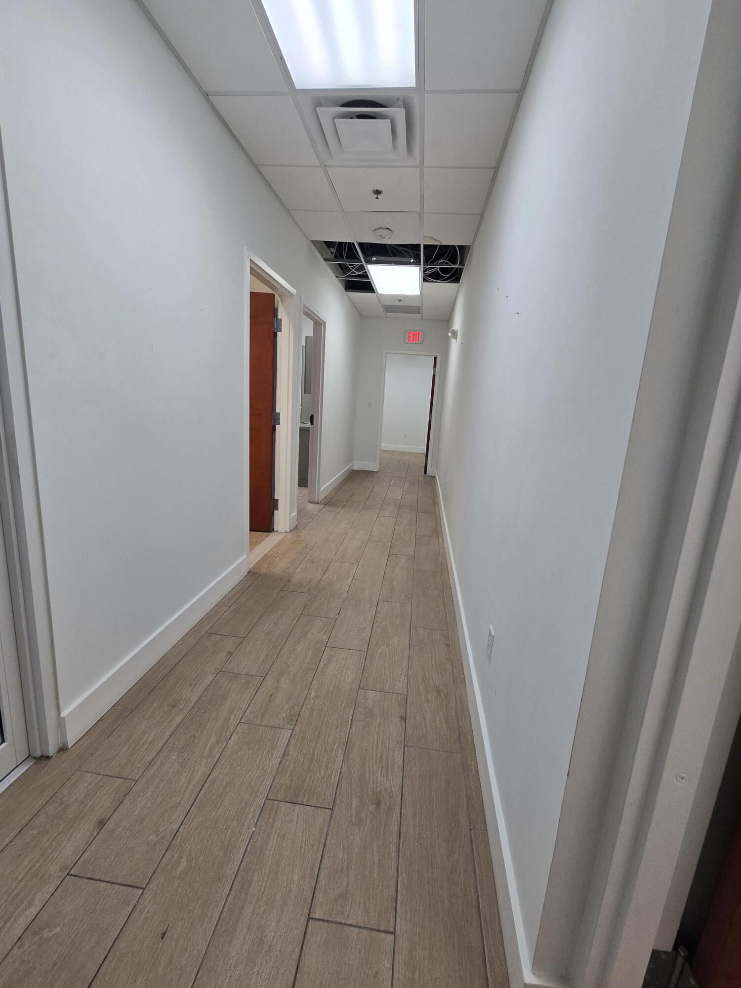 Commercial hallway with wood-look tile flooring and exposed wiring above missing ceiling tiles.