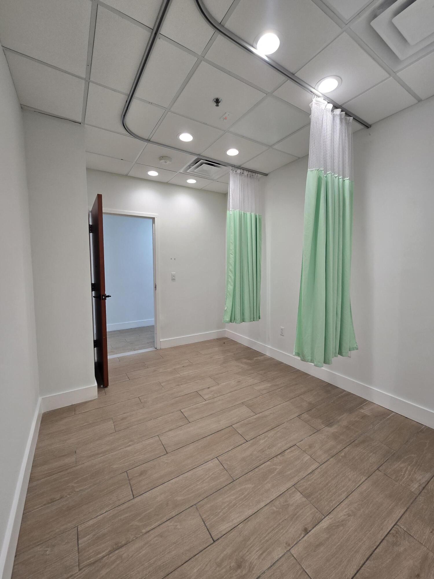 Empty treatment room with mint-green privacy curtains and wood-look tile flooring.
