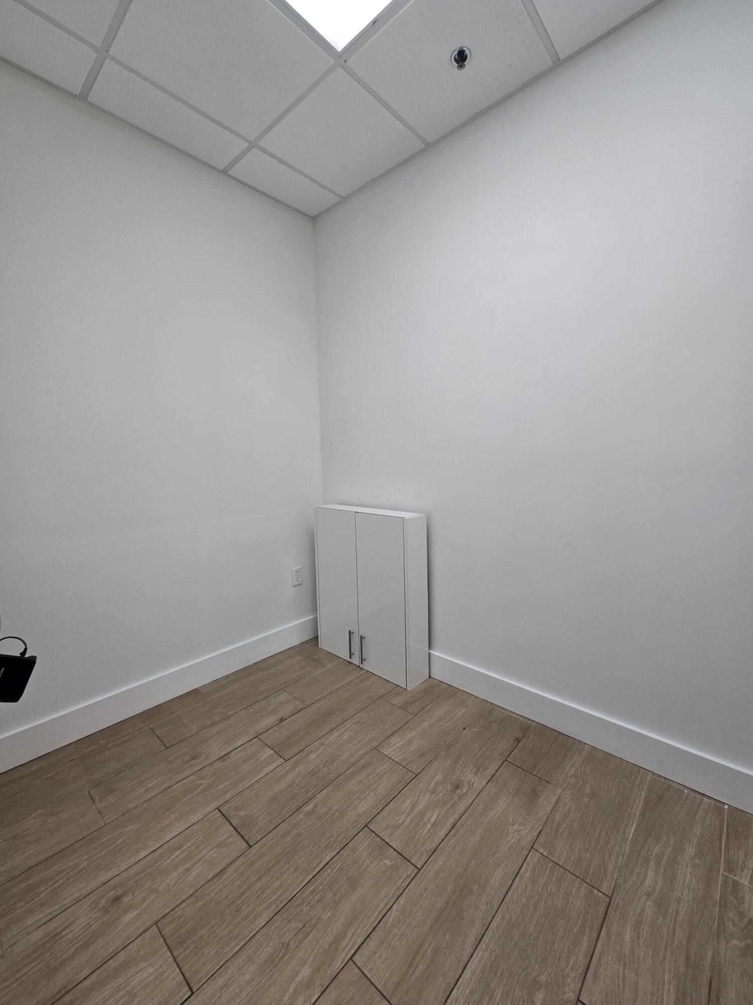 Vacant room with wood-look tile flooring and a small white cabinet in the corner.