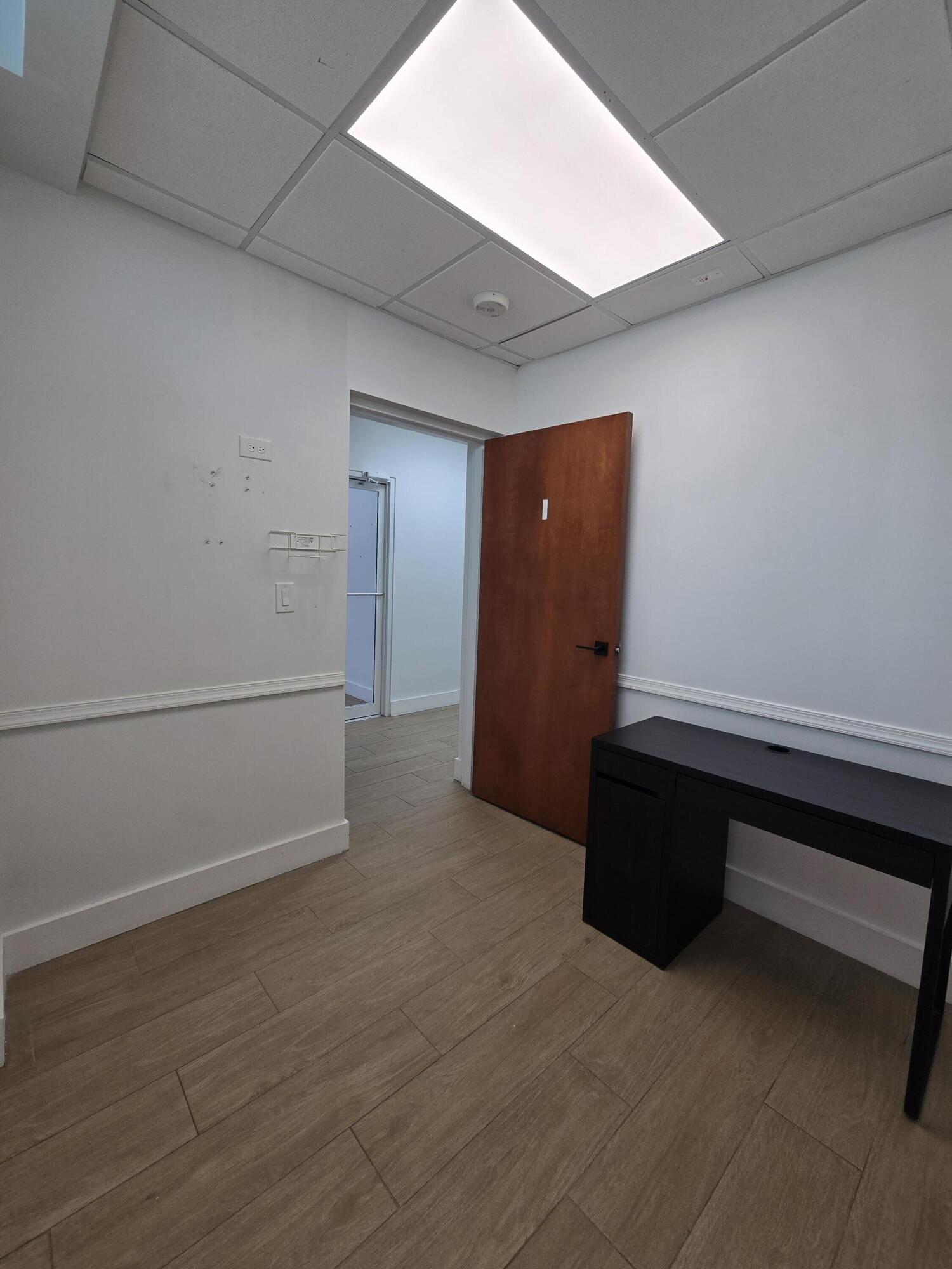 Small office with wood-look tile flooring, an open wooden door, and a black desk.