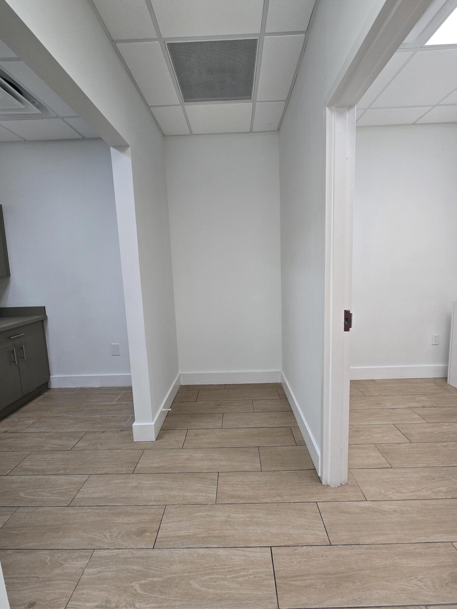 Empty commercial interior with brown tile floors, white walls, and openings to adjoining rooms.