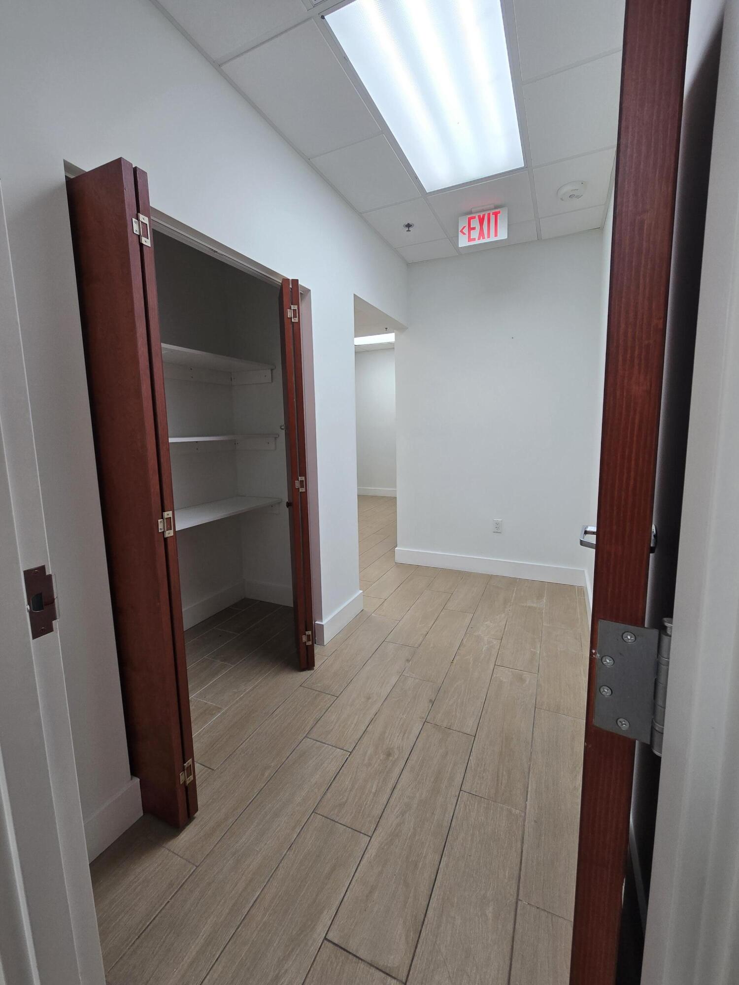 Empty commercial interior with tiled flooring, an open storage closet, and a lit EXIT sign.