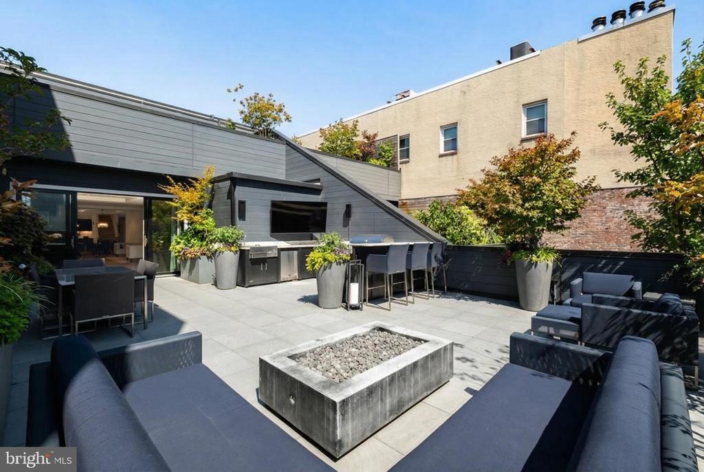 Rooftop terrace with gray seating, a stone fire pit, outdoor kitchen and planters.