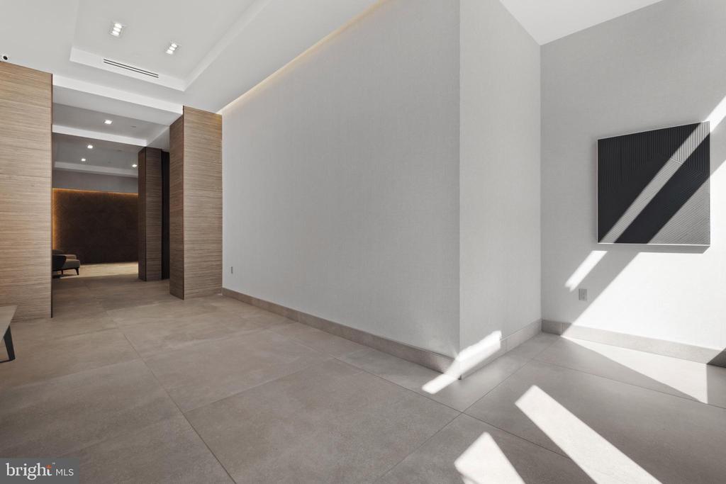 Modern entry hall with large gray tile floors, wood-paneled doorways, and geometric wall art.