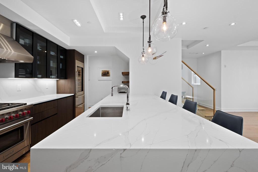 Modern kitchen with a large veined marble island, dark cabinetry, and stainless steel appliances.