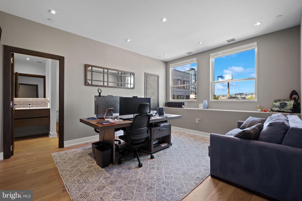Furnished home office with a computer desk, sofa, and two bright windows.