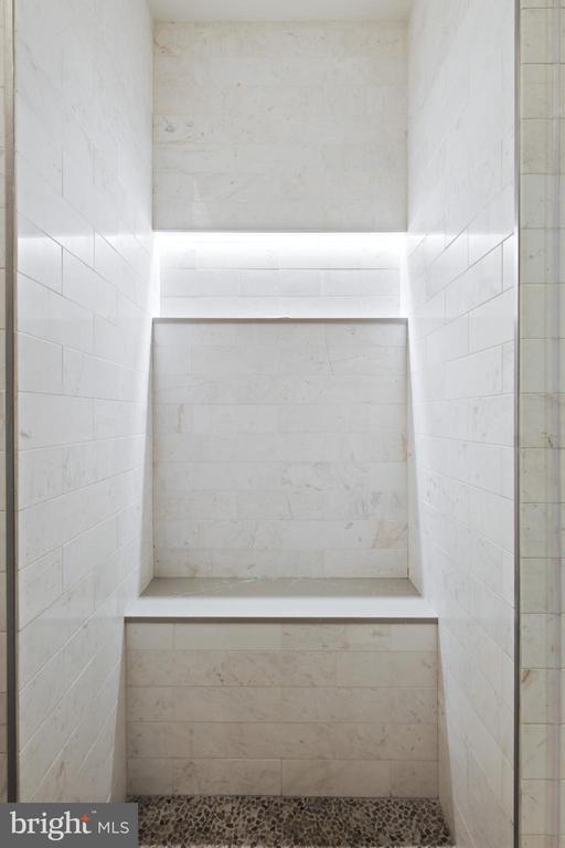 Walk-in shower with pale marble walls, built-in ledges, and a dark pebble floor.