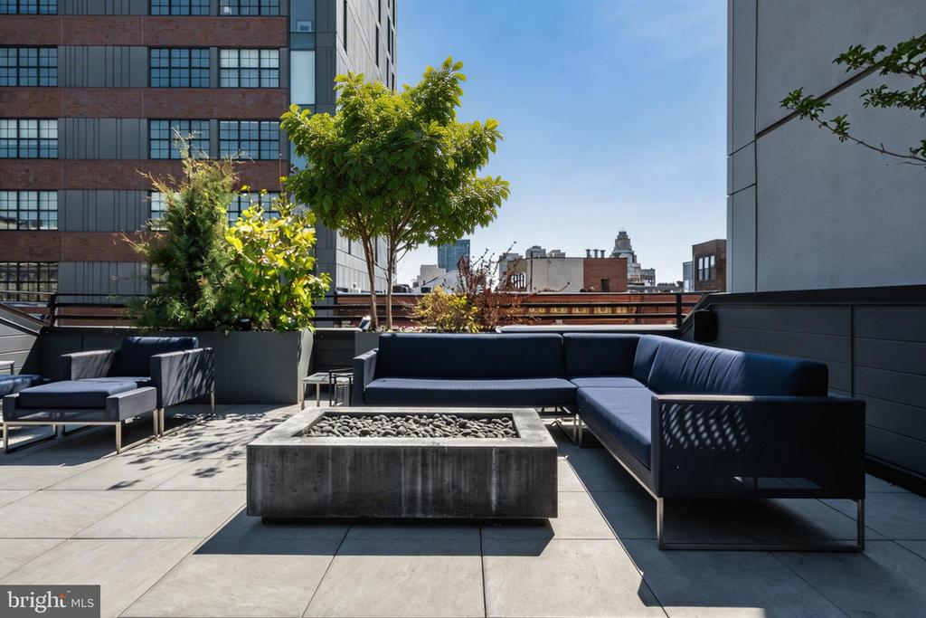 Rooftop terrace with blue sectional seating, a concrete fire pit, and Philadelphia buildings beyond.