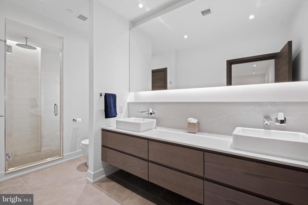 Modern bathroom with a glass shower and double vessel sinks above a dark wood floating vanity.