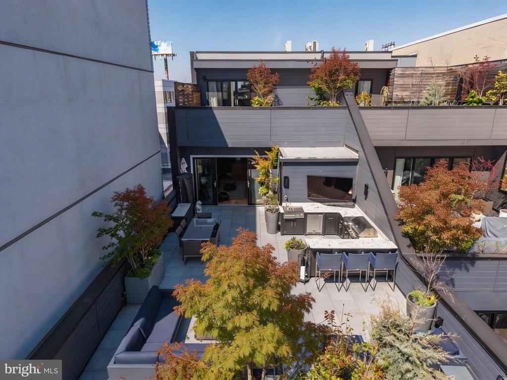 Rooftop terrace with an outdoor kitchen, bar seating, lounge furniture, and autumn planters.