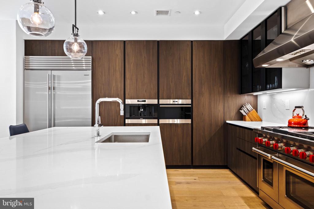 Modern kitchen with a large white island, dark wood cabinets, and stainless steel appliances.