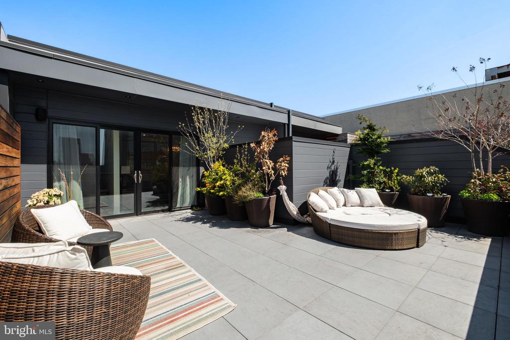 Rooftop terrace with woven lounge seating, potted plants, and sliding glass doors.