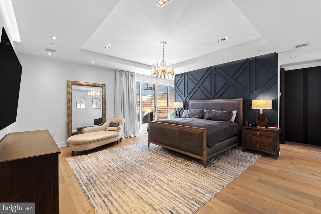 Furnished bedroom with a king bed, navy geometric feature wall, hardwood floors, and a window-side sitting area.