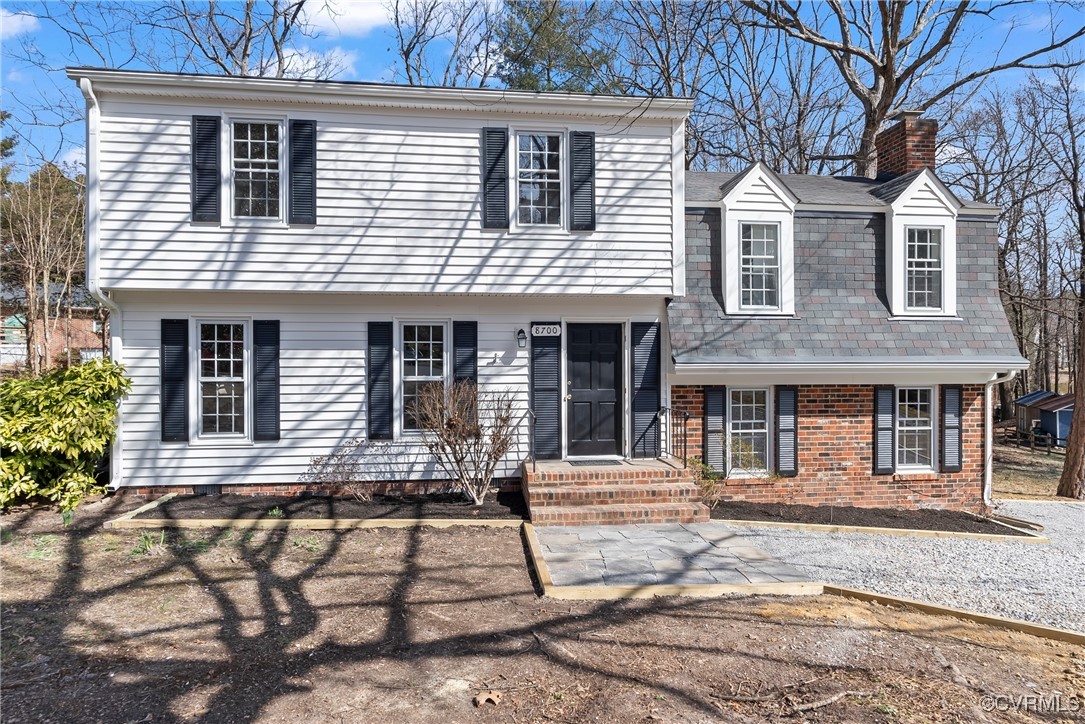 Two-story house with white siding, brick facade, roof dormers, and black shutters.