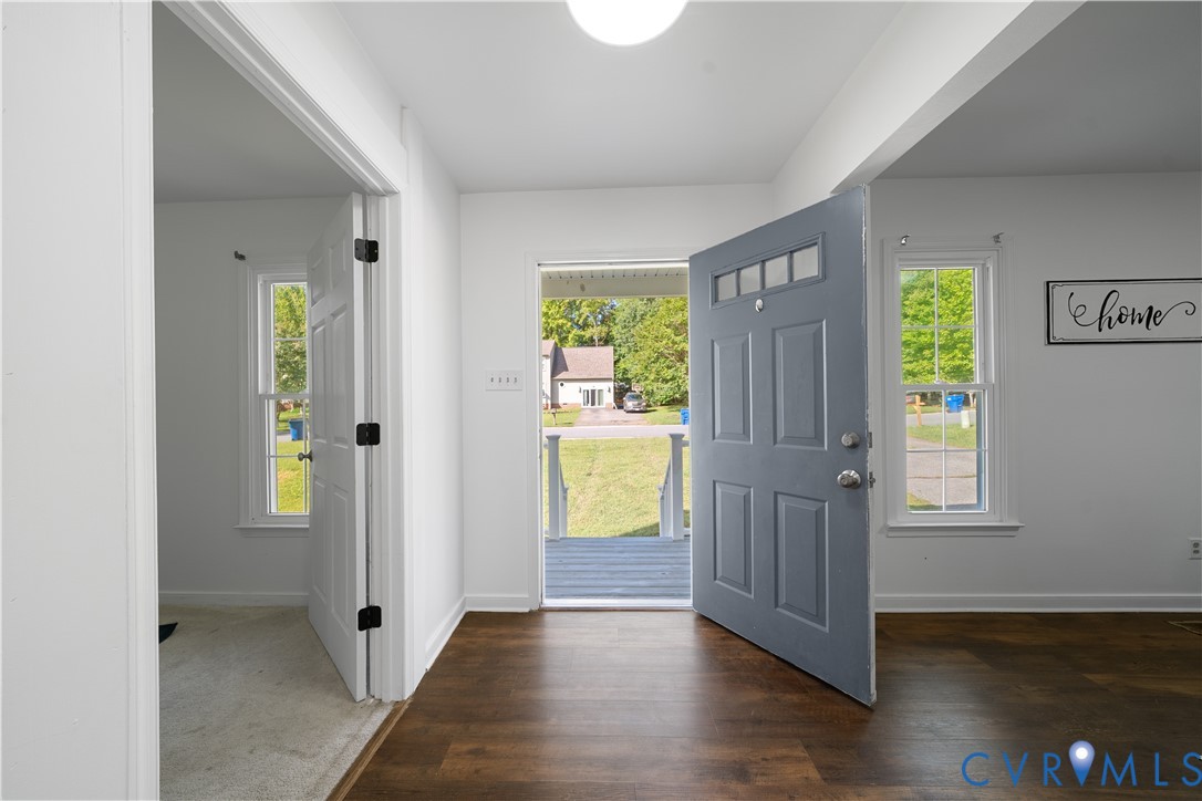 Entryway with dark hardwood floors and an open blue front door overlooking the porch and lawn.
